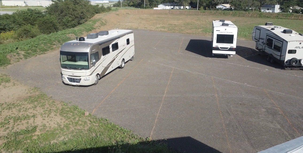 Motorhome and fifth-wheel trailers parked in marked angled stalls on the gravel lot.