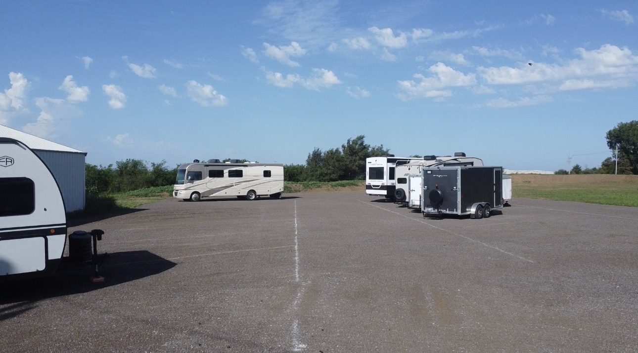 Wide view of the storage lot with motorhomes and enclosed trailers under an open sky.